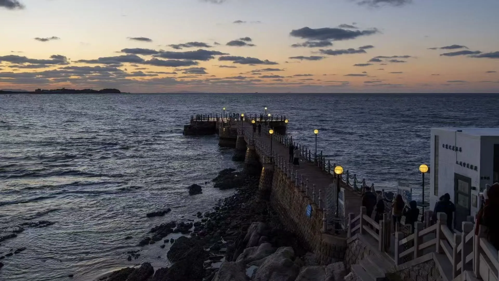 黄昏海岸边亮起灯光的石质栈桥 / A stone pier lit at dusk along the coast