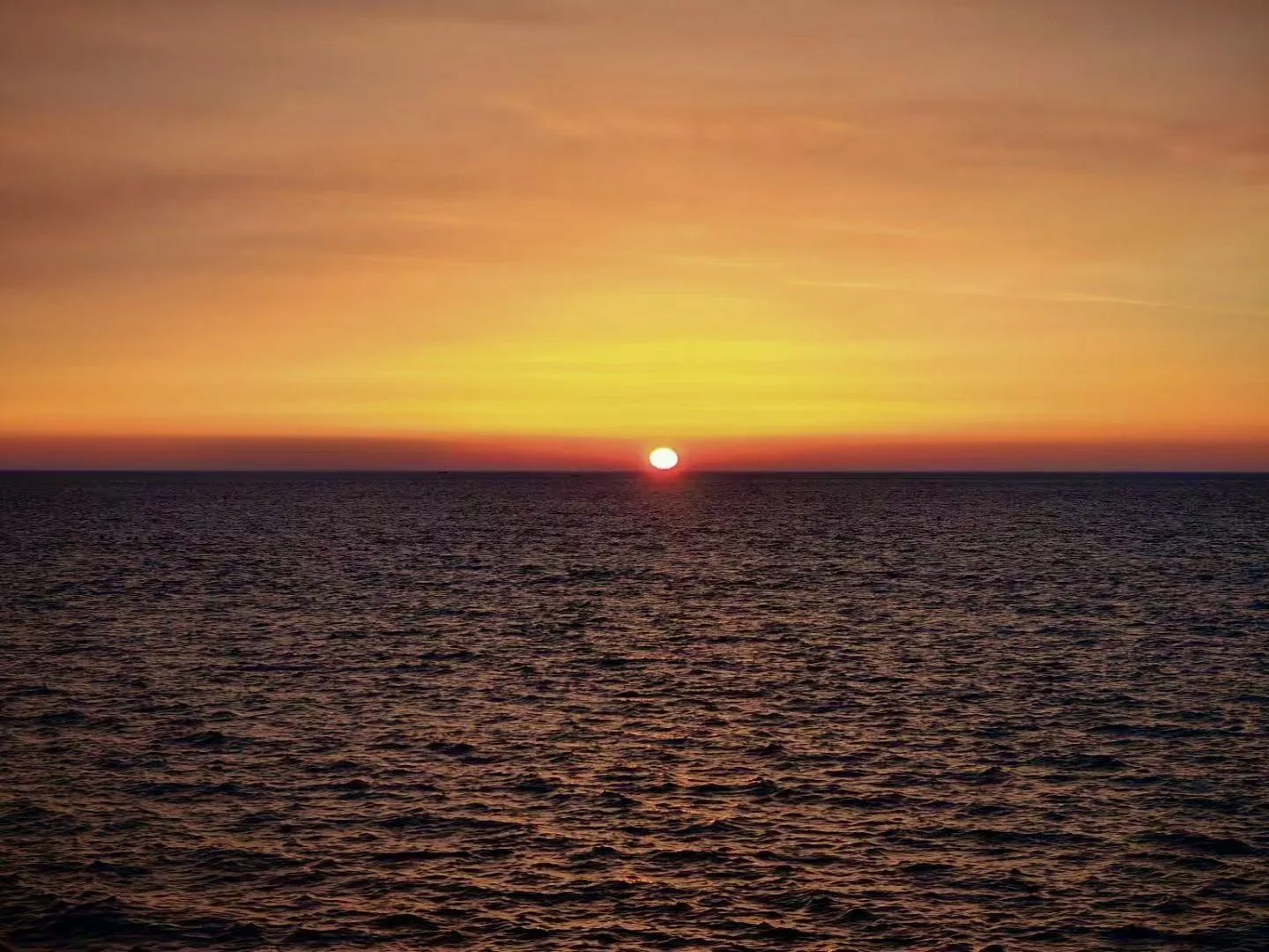 一轮红日从橙色海天交界处升起 / A red sun rising at the orange seam of sea and sky