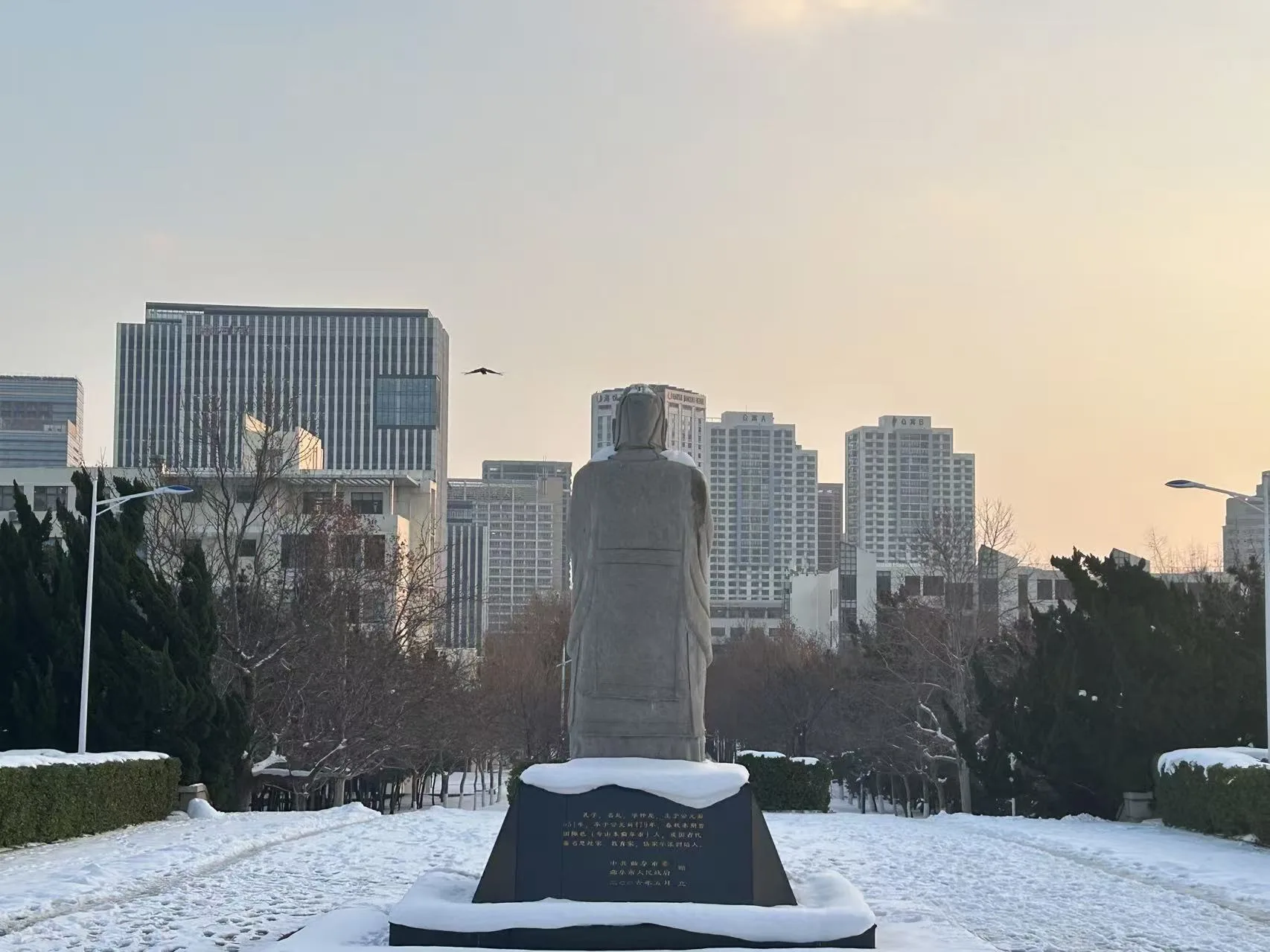 雪后校园中一座面向楼群的古人雕像 / A statue of an ancient figure facing campus buildings after snow
